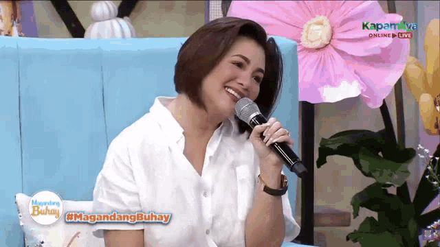 a woman is singing into a microphone while sitting on a blue couch ..