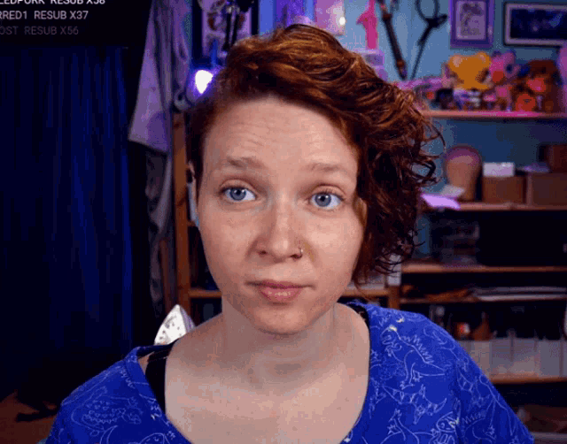 a woman in a blue shirt is looking at the camera with a sign behind her that says " redt resub x37 "