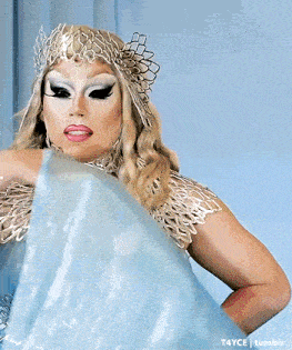 a drag queen wearing a blue dress and a silver crown is standing in front of a mirror
