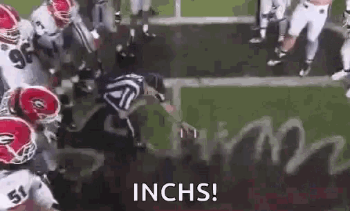 a group of football players are playing a game on a field and a referee is kneeling down on the field .