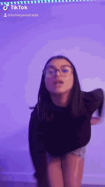 a woman wearing glasses is standing in front of a purple wall .
