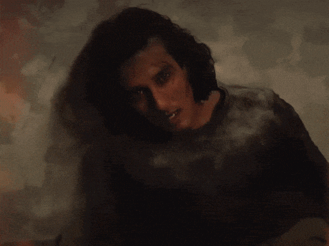 a man with long hair leaning against a white wall