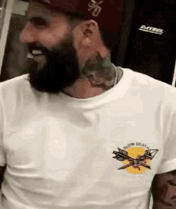 a man with a beard is wearing a hat and a white t-shirt .