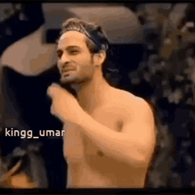 a shirtless man with a headband on his head is standing in front of a camera .