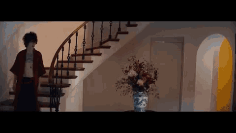 a man is walking down a set of stairs next to a vase of flowers on a table .