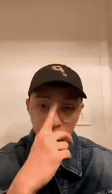 a man wearing a hat and glasses is covering his nose with his hand