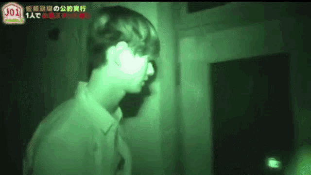 a man is standing in a dark room with a green light shining on his face .