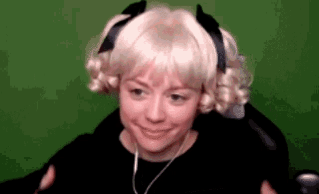 a woman wearing a blonde wig and headphones is sitting in front of a green screen and smiling .