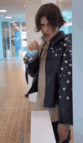 a man in a black leather jacket is drinking water from a bottle
