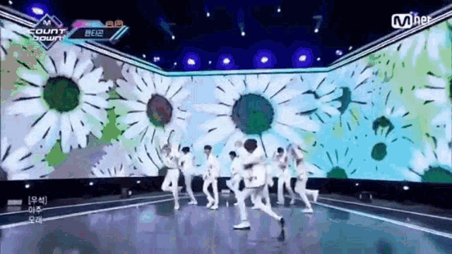 a group of young men are dancing on a stage in front of a large screen with flowers on it .