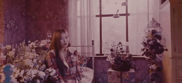 a woman is sitting in a room surrounded by flowers and a window .