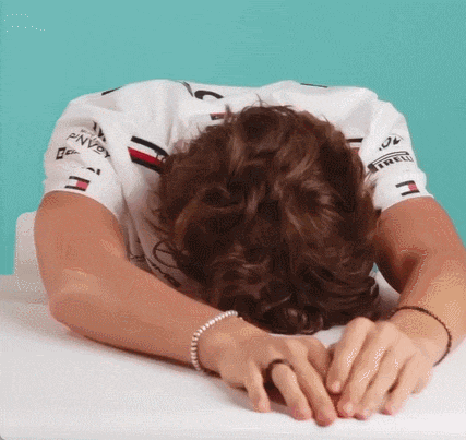 a man laying his head on a table with his hands on his face .