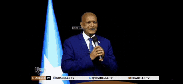 a man in a blue suit and tie holds a microphone in front of a banner for shabelle tv
