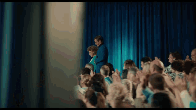a man and woman are standing on a stage in front of a crowd