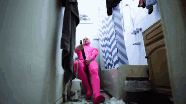 a man in a pink suit is sitting in a bathroom holding a toilet brush