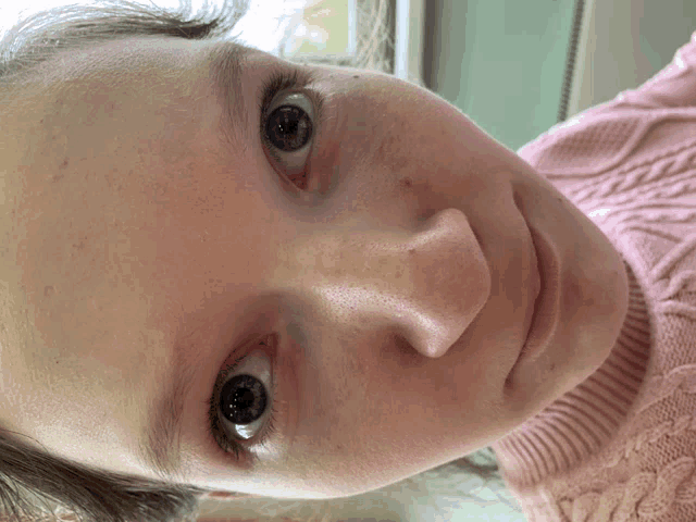 a close up of a girl 's face with a pink sweater