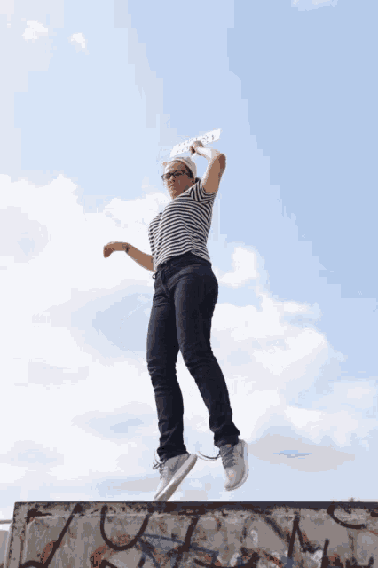 a woman in a striped shirt is jumping in the air while holding a piece of paper that says " love "