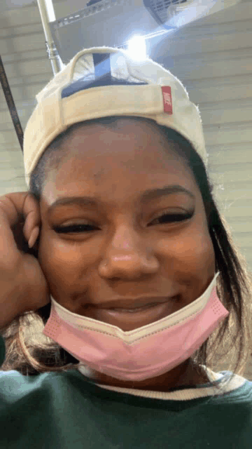 a woman wearing a nike hat and a pink face mask smiles