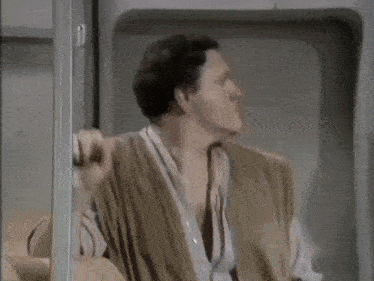 a man in a vest is standing in front of a door and looking out .