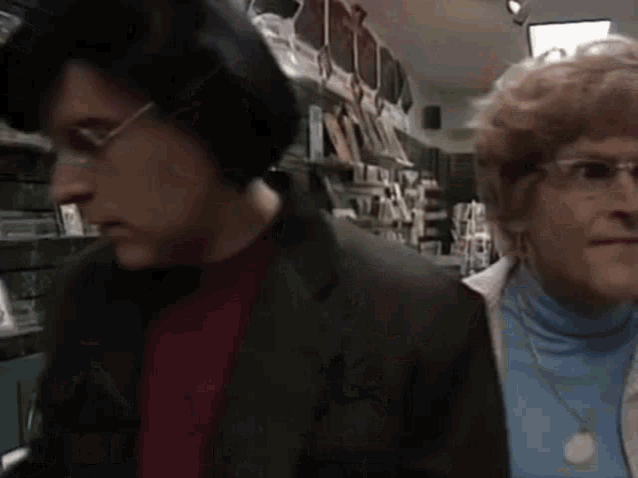 a man and a woman are walking in a store . the woman is wearing glasses .