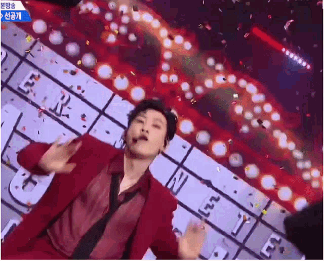 a man in a red suit is dancing on a stage with confetti falling around him .