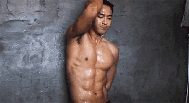 a shirtless man is taking a shower in front of a wall