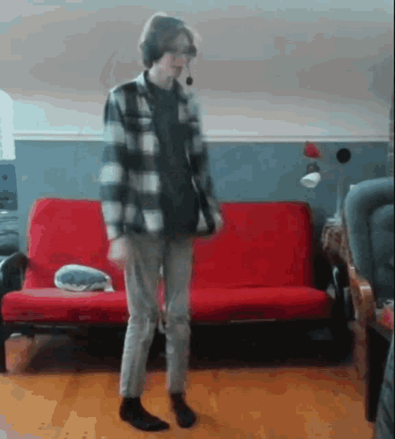 a person in a plaid shirt is dancing in front of a red futon