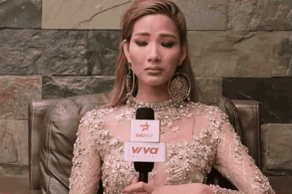a woman in a gold dress is sitting in a chair with a microphone on her neck .