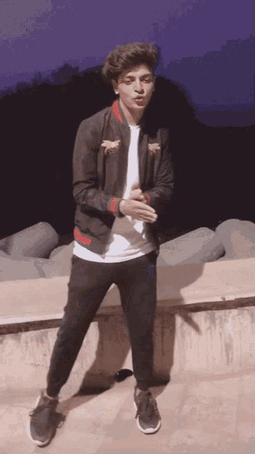 a young man wearing a black jacket and black pants is standing on a wall
