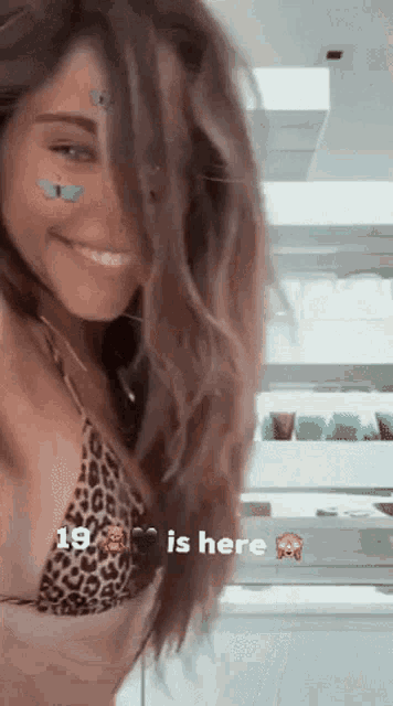 a woman in a bikini with a butterfly on her face is smiling and the number 19 is here