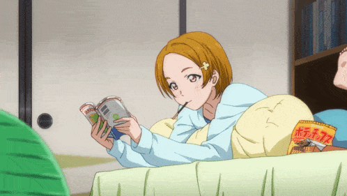 a girl is laying on a bed reading a book and eating a snack