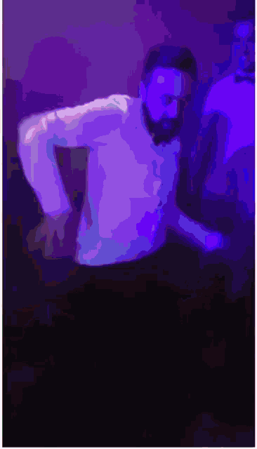 a man with a beard is dancing in a dark room with purple lights .