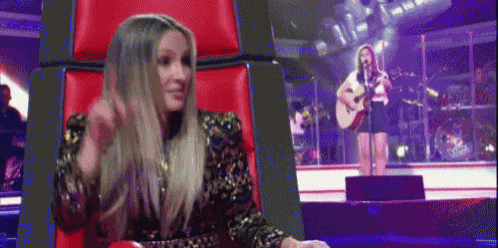 a woman is sitting in a red chair watching a woman sing on stage .