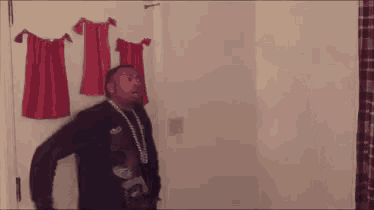a man in a hat is standing next to a man in a black shirt in a room with red towels on the wall .