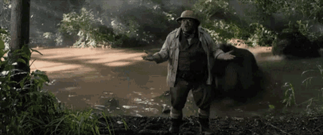 a man in a hat is standing next to a large animal in a river .