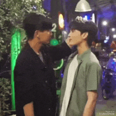 a couple of men are standing next to each other on a street and one of them is touching the other 's face .