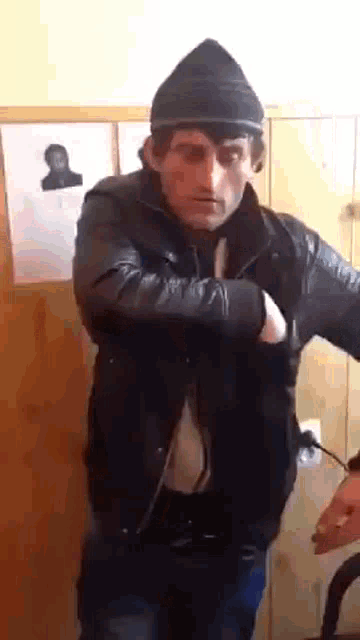 a man wearing a black hat and a leather jacket is standing in front of a wall .