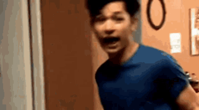 a man in a blue shirt is making a funny face while standing in front of a door .