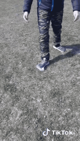 a man in camouflage pants is walking on a grassy field with a tik tok watermark