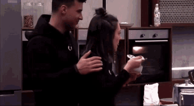 a man is hugging a woman in a kitchen while she looks at something in an oven
