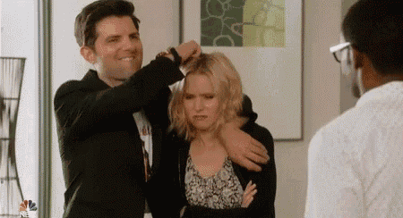 a man is putting a woman 's hair in a ponytail while a woman looks on .