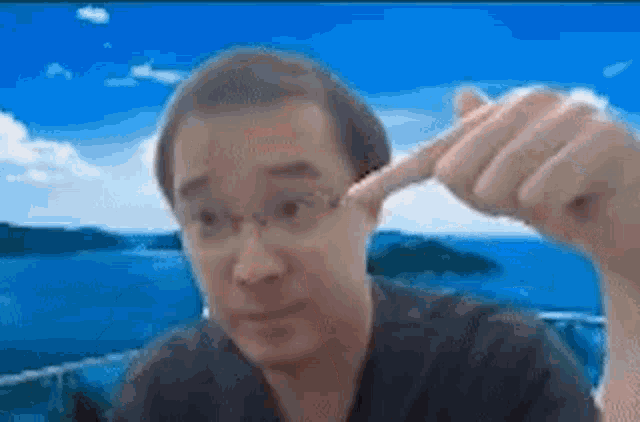 a man with glasses is making a funny face and pointing at his head .