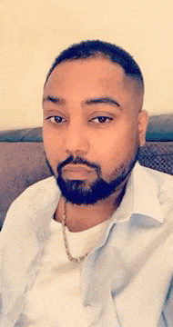 a man with a beard and a necklace is sitting on a couch .