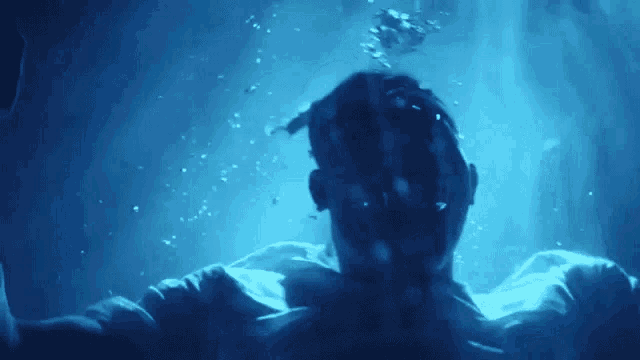 a man is swimming underwater in a dark room with bubbles coming out of the water .