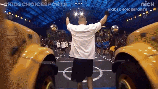 a man stands on a basketball court with his arms in the air in front of school buses .