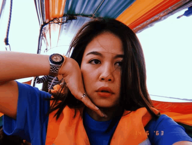 a woman wearing a blue shirt and an orange vest has a watch on
