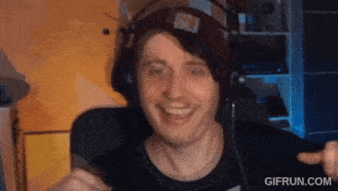 a man wearing headphones and a beanie is smiling in front of a computer screen .