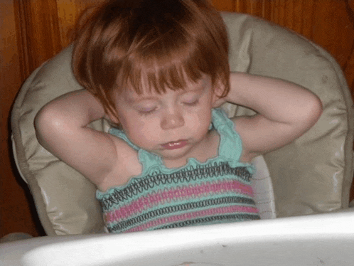 a little girl sitting in a high chair with her hands behind her head