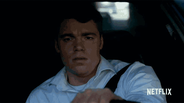 a man in a white shirt is driving a car with netflix written on the bottom of the screen
