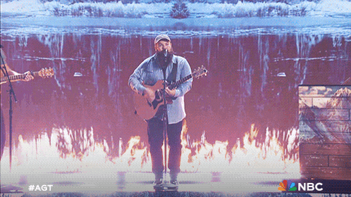 a man singing and playing a guitar on a stage with a nbc logo behind him